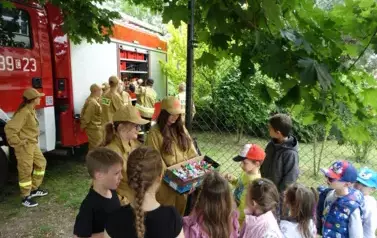 młodziki ze straży pożarnej częstują słodkościami uczni&oacute;w szkoły