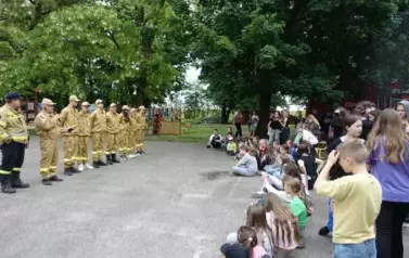 strażacy z OSP, dzieci siedzące na boisku