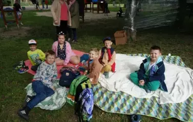 uczniowie siedzący na rozłożonych kocach