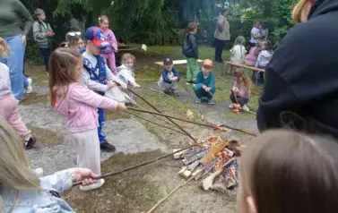 dzieci pieką kiełbaski przy ognisku