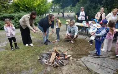 dzieci i nauczyciele pieką kiełbaski przy ognisku