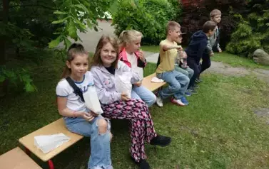 dzieci siedzą na ławeczce i zajadają przekąski