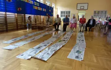 Seniorzy uczestniczący w zabawie sprawnościowej z gazetą
