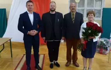 Pani Dyrekotr trzymająca w ręku bukiet 25 czerwonych r&oacute;ż z przedstawicielami pracownik&oacute;w szkoły