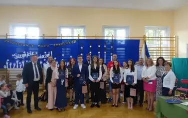 absolwenci trzymający świadectwa z wyr&oacute;żnieniem wraz z rodzicami, wychowawcą, Panią Dyrektor i Panem Burmistrzem