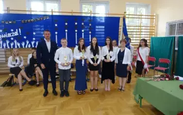 absolwenci trzymający w rękach statuetki z nauczycielem i Panią Dyrektor
