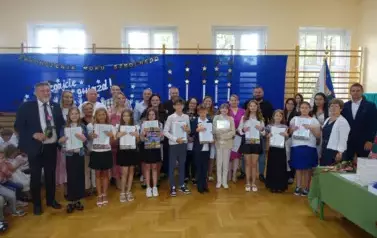 uczniowie trzymający świadectwa z wyr&oacute;żnieniem wraz z rodzicami, wychowawcą, Panią Dyrektor i Panem Burmistrzem