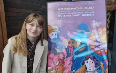dziwczynka na tle plakatu reklamującego konkurs plastyczny