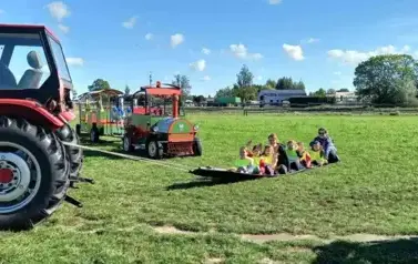 traktor ciągnie plandekę, na kt&oacute;rej siedzą dzieci i dwie osoby dorosłe