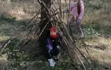 dziwczynka i chłopiec budujący szałas z gałęzi
