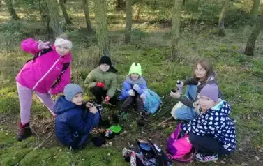 dzieci jedzące śniadanko na trawie w lesie