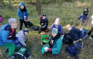 dzieci jedzące śniadanko na trawie w lesie