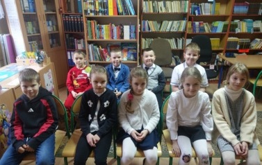 pierwszoklasiści czekający na pasowania na czytelnika, w tle p&oacute;łki z książkami
