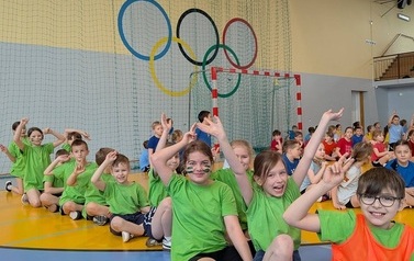 dzieci w zielonych koszulkach podczas zawod&oacute;w sportowych, podnoszące ręcę do g&oacute;ry
