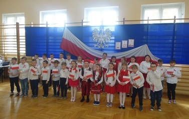 uczniowie klas I-III ubrani oświętnie trzymający małe flagi Polski