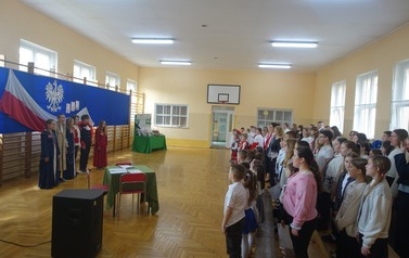 społeczność uczniowska stojąca na baczność i śpiewająca Hymn Polski