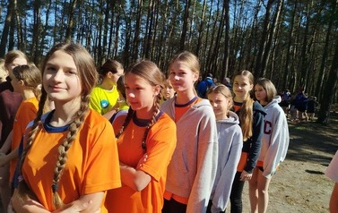 drużyna dziewcząt stojąca na zbi&oacute;rce przed rozpoczęciem zawod&oacute;w sportowych, w tle lasek