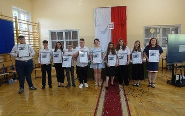 Absolwenci wraz z wychowawczynią trzymający w rękach zdjęcie w ramce wydrukowanej strony z gazety.
