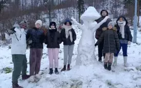 grupa uczni&oacute;w z wolanturieszem przy figurze ze śniegu