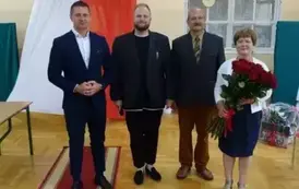 Pani Dyrekotr trzymająca w ręku bukiet 25 czerwonych r&oacute;ż z przedstawicielami pracownik&oacute;w szkoły