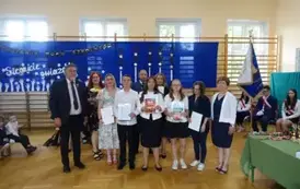 uczniowie trzymający świadectwa z wyr&oacute;żnieniem wraz z rodzicami, wychowawcą, Panią Dyrektor i Panem Burmistrzem