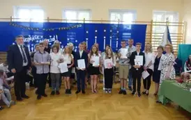 uczniowie trzymający świadectwa z wyr&oacute;żnieniem wraz z rodzicami, wychowawcą, Panią Dyrektor i Panem Burmistrzem
