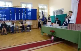 Pani Dyrektor przemawia przez mikrofon, w tle zaproszeni goście, poczet sztandarowy i absolwenci
