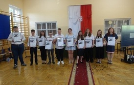 Absolwenci wraz z wychowawczynią trzymający w rękach zdjęcie w ramce wydrukowanej strony z gazety.