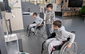 Dw&oacute;jka chłopc&oacute;w korzystających ze stacjonarnych w&oacute;zk&oacute;w inwalidzkich, trzeci chłopiec przygląda się im