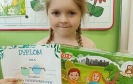 dziewczynka trzymająca w rękach dyplom i upominek za udział w konkursie