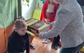 Pani Dyrektor pasuje ucznia klasy I na czytelnika.Dotyka wielką książką ramienia dziecka.