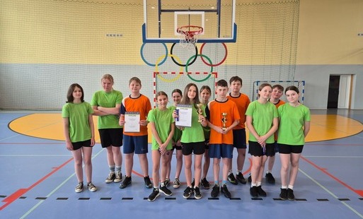 drużyny dziewcząt i chłopców z pucharami za I miejsce po Zawodach w Koszykówce na hali sportowe, w tle znak olimpijski